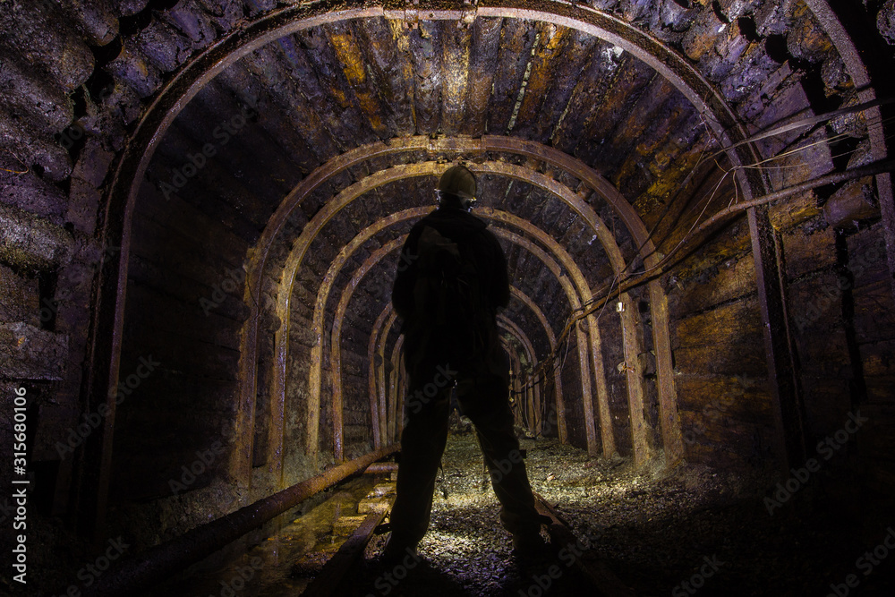 Miner in the dark mine tunnel with timbering