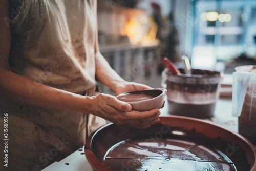 Female ceramic maker in a linen brown apron working in pottery workshop glazing bowl, Handcraft Creative People 
