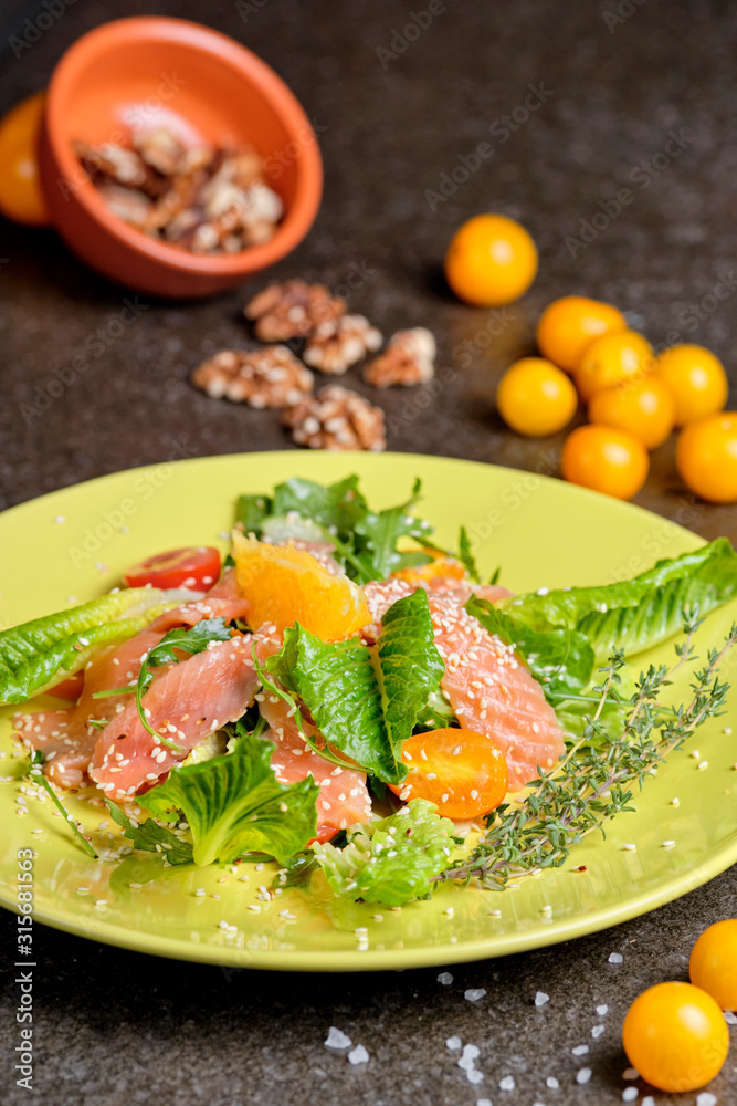 Cold salmon salad with green leaves, cucumber, avocado, lime and tomato on black stone background. Top view with copy space. Rustic style.