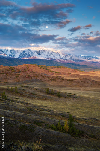 The moon over the North Chuysky ridge, dawn. Autumn in the Altai mountains. Russia
