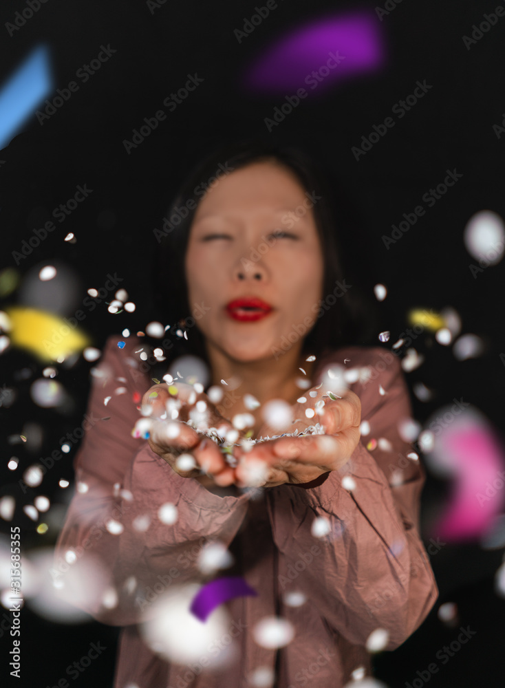 Woman blow confetti from her hand. Focus is on the confetti. Woman blow confetti from her hand. Focus is on the confetti.