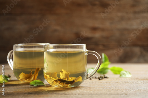 Cups of green tea and leaves on wooden table