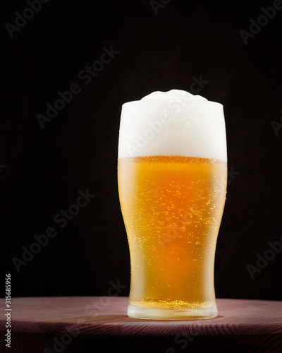 A glass of light beer with foam on a black background.