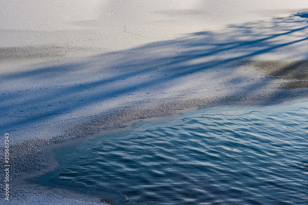 A beautiful winter or spring scene of sun having melted a water hole into a frozen lake A beautiful winter or spring scene of sun having melted a water hole into a frozen lake