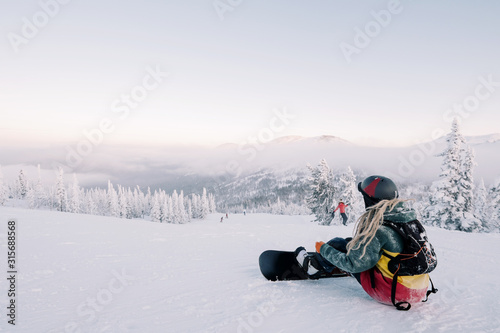 sitting female snowboarder wearing long hair preparing for riding from mountain top