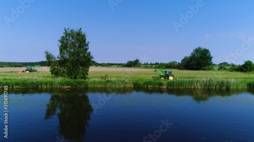 Aerial view of two tractor cutting grass by a lake