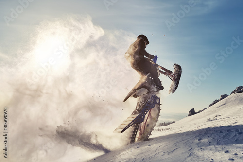 Snowbike rider jumping in mountain valley. Modify dirt bike with snow splashes and trail. Snowmobile sport riding photo