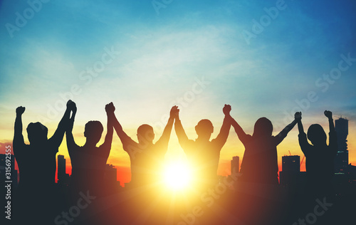Silhouette of group business team making high hands over head in sunset sky in city for business success and teamwork