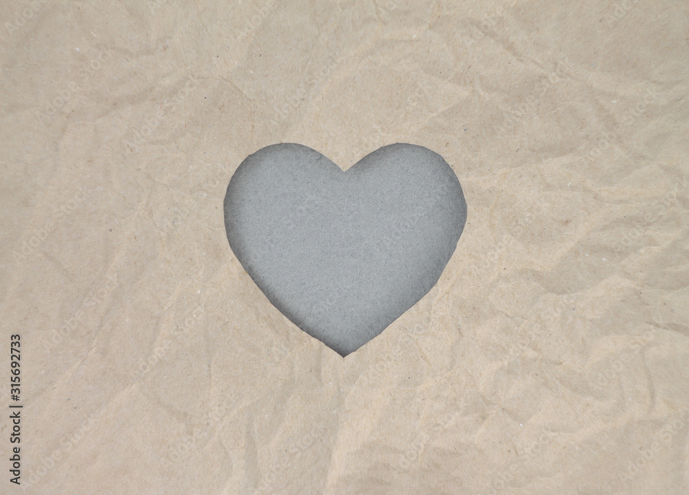 Fototapeta premium Gray felt heart on craft paper. Crumpled paper texture. Valentine's day stock photo for web, print and wallpaper. With empty space for text.