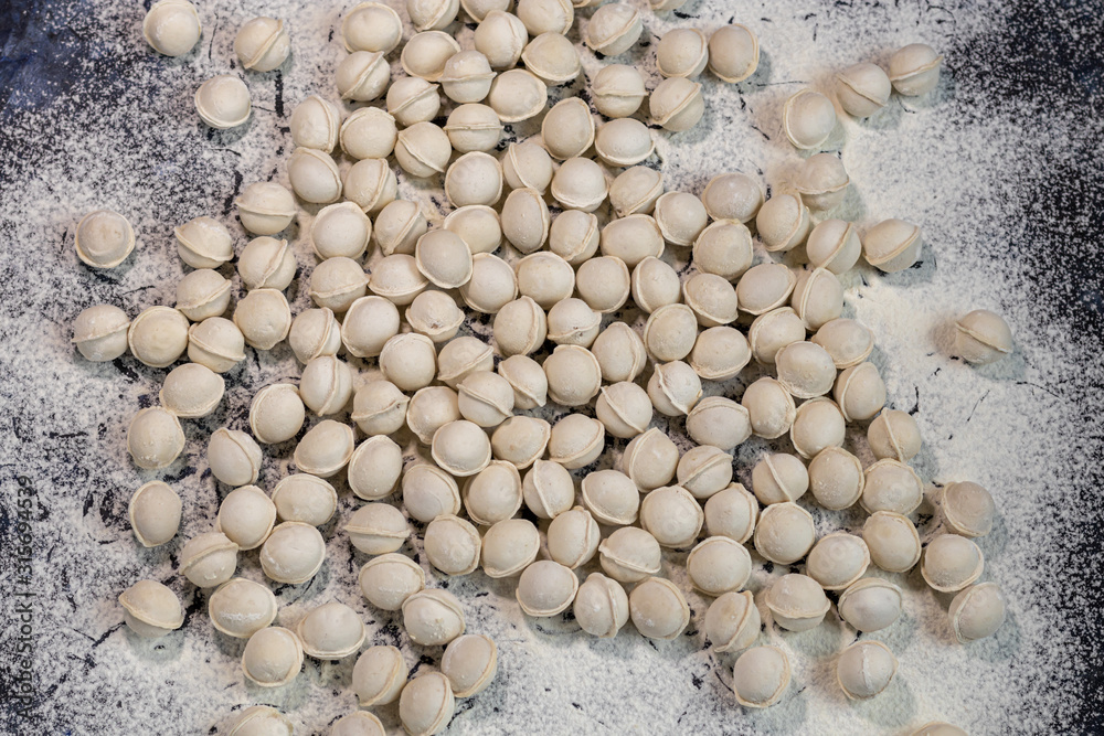 Flour pours onto the table. In order to make dough products, mini-dumplings are not stuck. Dumplings fall into flour. Dark marbled background. Flour pours onto the table. In order to make dough products, mini-dumplings are not stuck. Dumplings fall into flour. Dark marbled background.