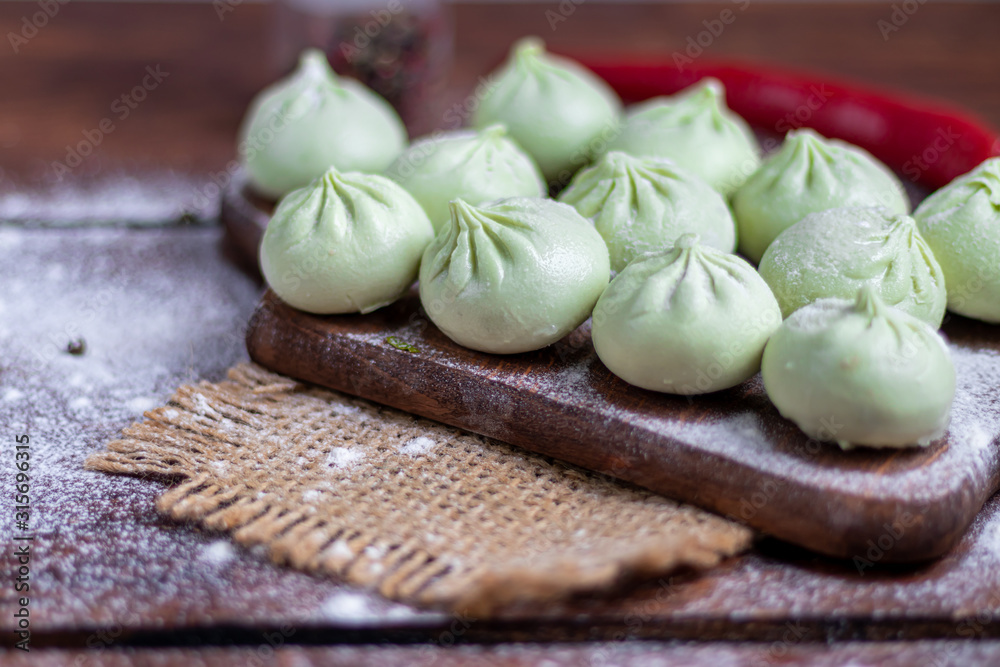 Frozen dough khinkali with spinach. Garnished with Red Chilli, Dill and Parsley. On a wooden background. Frozen dough khinkali with spinach. Garnished with Red Chilli, Dill and Parsley. On a wooden background.
