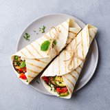 Wrap sandwich with grilled vegetables and feta cheese on a plate. Grey background. Top view
