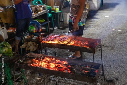 LABUAN BAJO, FLORES/ INDONESIA - NOVEMBER 3, 2019: Man cooking fish on grill at Night fish market at Labuan Bajo photo