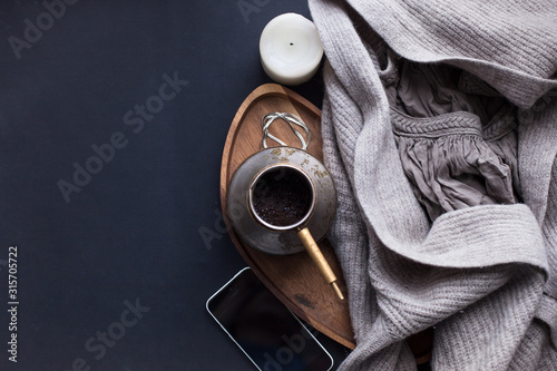 Winter cozy concept. Flatlay of gray knitted sweater, candle, coffee drink, diary, phone, glasses on black table. Warm weekend in cold weather. dark atmosphere