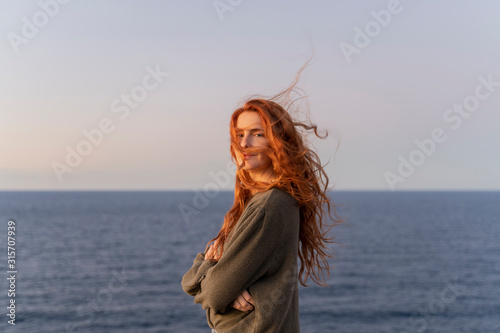 Portrait of redheaded young woman with windswept hair at the coast at sunset, Ibiza, Spain
