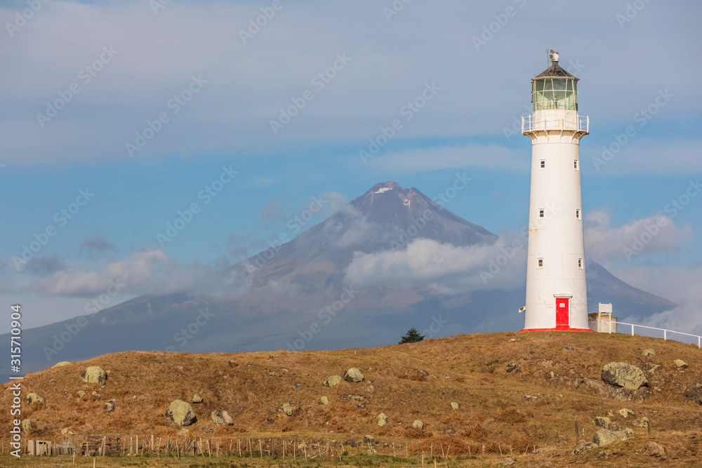 New Zealand, South Taranaki District, Pungarehu, Cape Egmont Lighthouse with Mount Taranaki volcano in background New Zealand, South Taranaki District, Pungarehu, Cape Egmont Lighthouse with Mount Taranaki volcano in background
