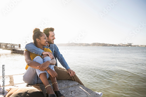 Young couple sitting on pier at the waterfront enjoying the view, Lisbon, Portugal photo