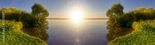 Beautiful view of lake with shore overgrown with reeds in sunny day. Rest in nature. Panoramic banner. Landscape on sunrise.