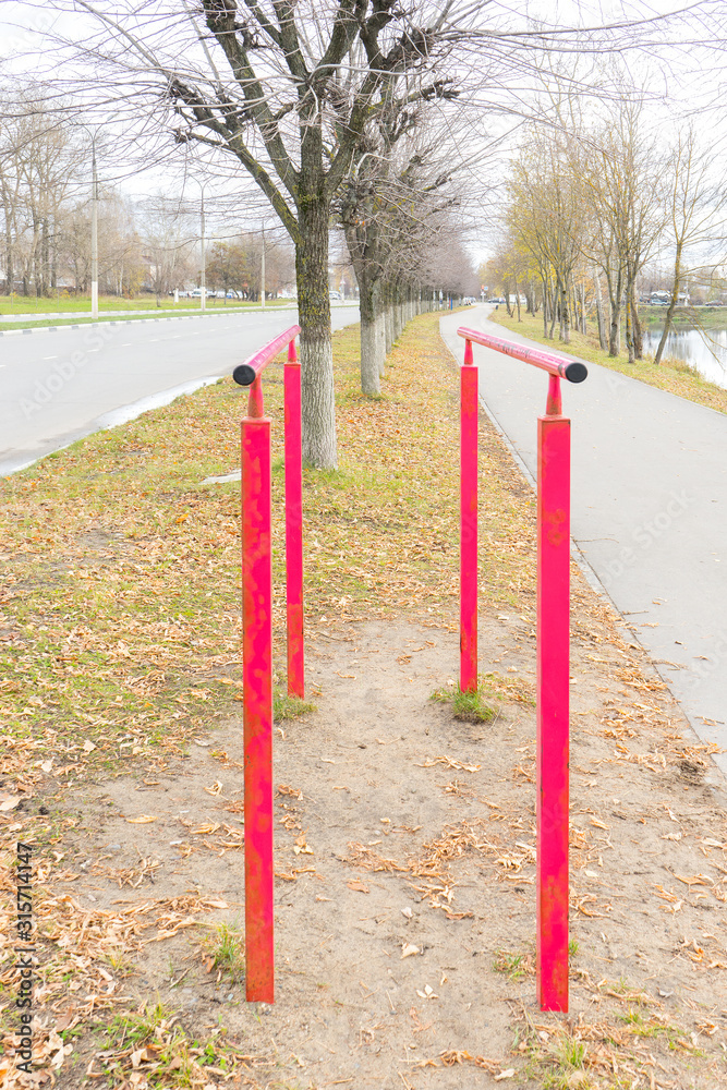 Iron, painted parallel bars for pulling up are installed on embankment near roadway. Sports equipment. Autumn landscape. Healthy lifestyle