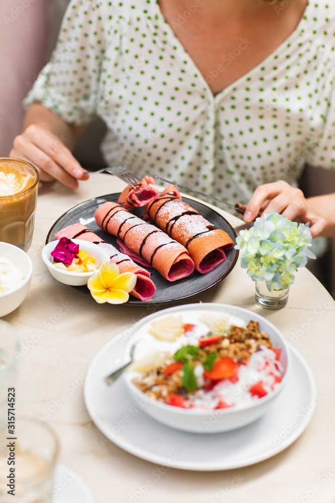 Woman eating delisious pink crispy pancake. It made from pitaya - dragon fruit. Fresh homemade crepes with chocolate sauce on marble table. Woman eating delisious pink crispy pancake. It made from pitaya - dragon fruit. Fresh homemade crepes with chocolate sauce on marble table.