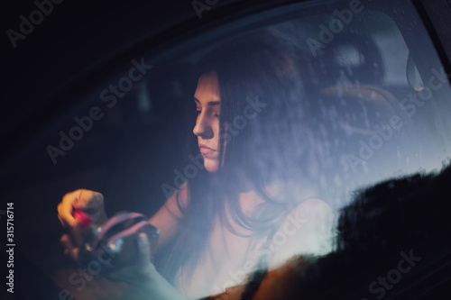 Fototapeta Naklejka Na Ścianę i Meble -  Young woman puts on makeup inside a car at sunset