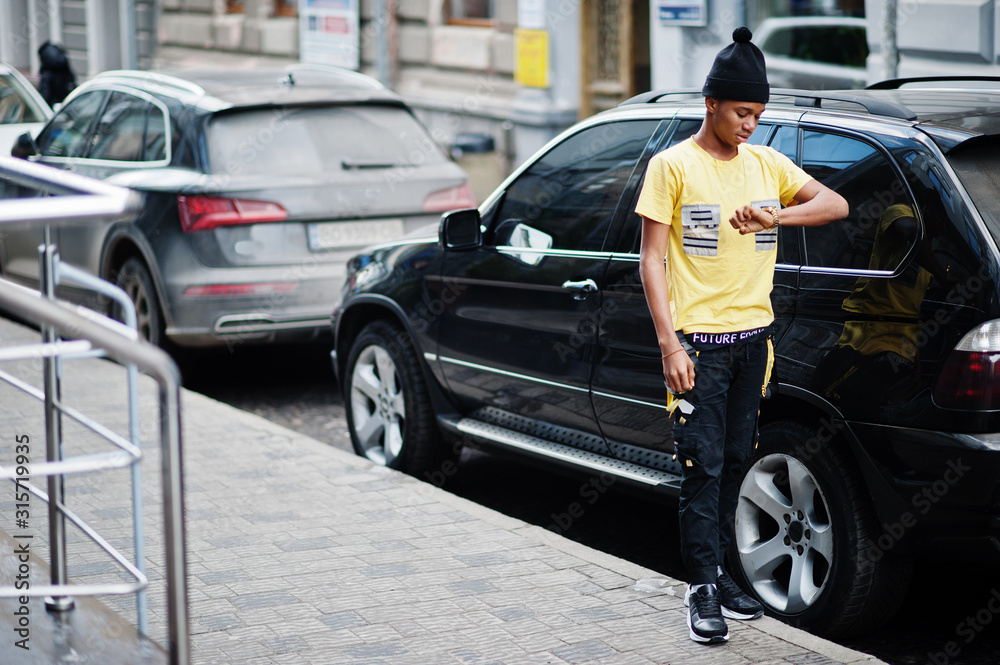 African man wear on black hat posed outdoor against business car. African man wear on black hat posed outdoor against business car.