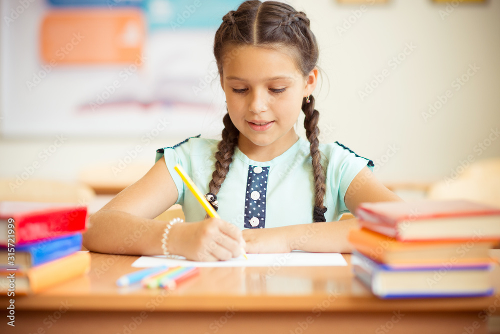 Portrait of pretty schoolgirl sitting at desk with many books in classroom Portrait of pretty schoolgirl sitting at desk with many books in classroom