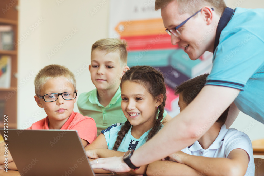 Young handsome teacher with group of clever children working with laptop during a lesson