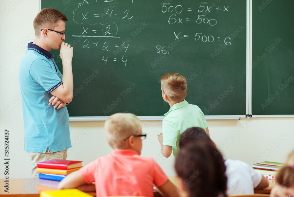 Young male teacher explaining math at the blackboard during a lesson at school Young male teacher explaining math at the blackboard during a lesson at school