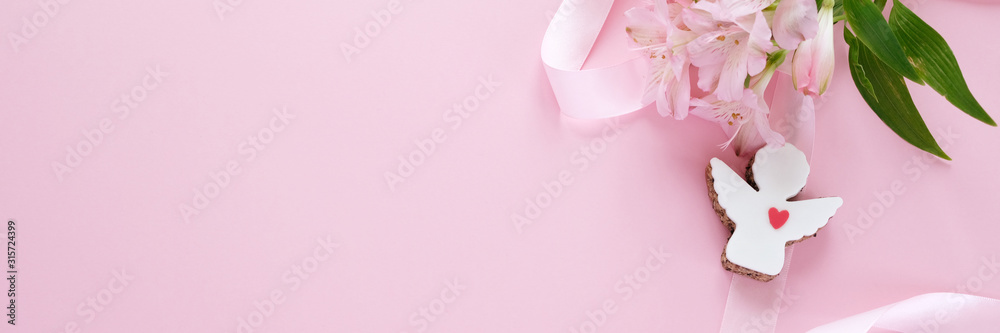 Cookies in the shape of an angel with a pink ribbon with lisianthuses on a pink background.