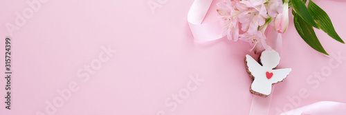 Cookies in the shape of an angel with a pink ribbon with lisianthuses on a pink background. © EkaterinaVladimirova