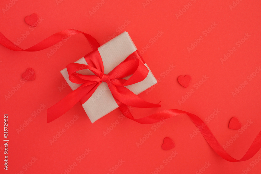 Gift with red bow and red hearts on the red background. Top view. Copy space. Gift with red bow and red hearts on the red background. Top view. Copy space.