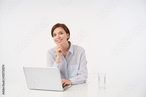 Wallpaper Mural Positive young brown-eyed brunette female with casual hairstyle keepig raised hand on her chin and looking cheerfully aside with charming smile, sitting over white background Torontodigital.ca
