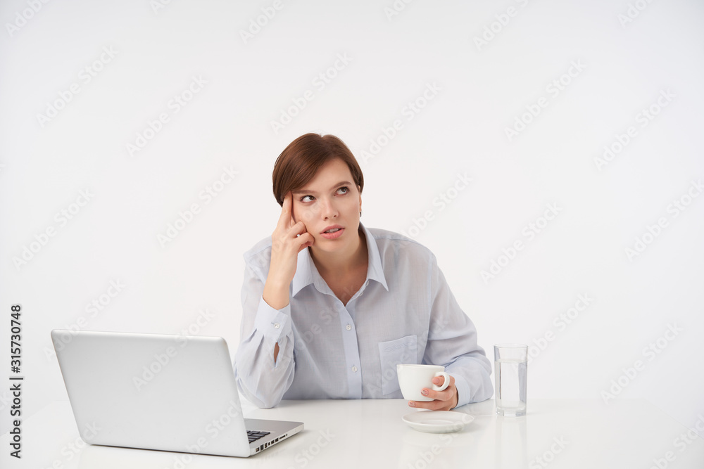Bored young pretty short haired brunette lady leaning her head on raised hand and rolling drearily eyes, wearing formal clothes while posing over white background Bored young pretty short haired brunette lady leaning her head on raised hand and rolling drearily eyes, wearing formal clothes while posing over white background