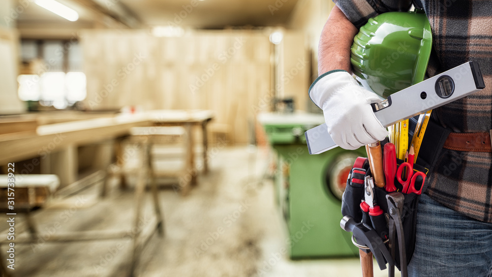Close-up. Carpenter with hands protected by gloves holds helmet and level. Construction industry, carpentry workshop. - obrazy, fototapety, plakaty 