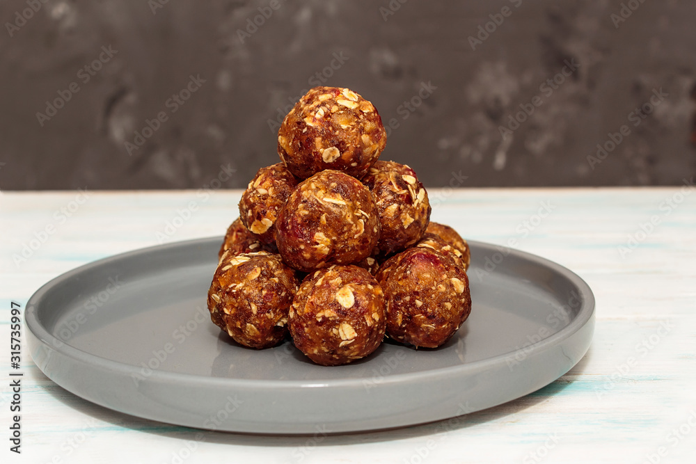 Homemade energy balls like a healthy breakfast or a snack of raisins, dried apricots, dates, nuts and oatmeal, thet lie on a gray ceramic plate on a white wood background. Horizontal orientation. Homemade energy balls like a healthy breakfast or a snack of raisins, dried apricots, dates, nuts and oatmeal, thet lie on a gray ceramic plate on a white wood background. Horizontal orientation.