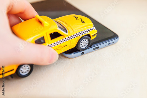 Smartphone application of taxi service for online searching calling and booking cab concept. Hand holding yellow toy car Taxi Cab on empty screen of smart phone on wooden background. Taxi symbol.
