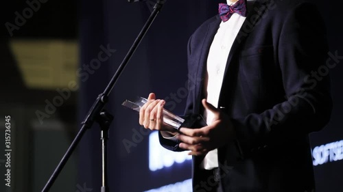 Middle shot of business man winner holding a glass statue prize enjoying a victory and making grateful speech on stage performance. Award ceremony.