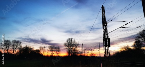 A fantastic sunset with red yellow orange and purple tones with dramatic cloud formation over green meadows with bare trees in January on the island of Rügen