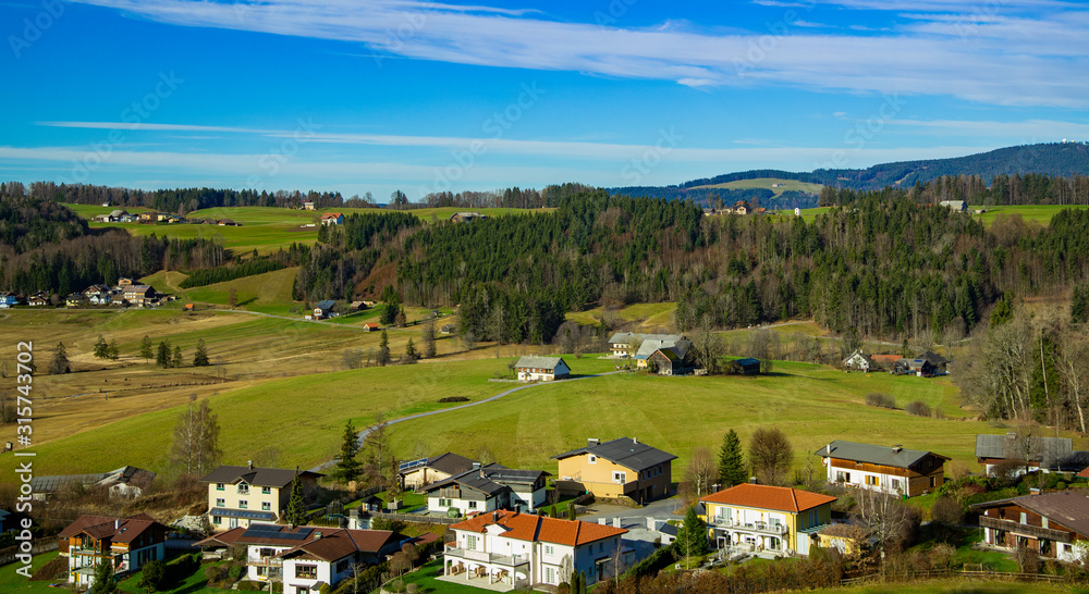 aerial landscape top view of European village country side Austrian outskirts landmark houses on highland spring time valley with green grass and trees foliage with horizon background line blue sky
