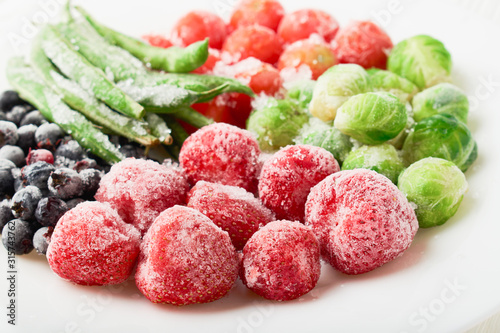 White plate with frozen food in a plate - strawberries with shadberry and brussels sprouts with asparagus beans photo