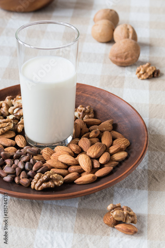 healthy eating concept, almonds, pine nuts, walnuts and a glass of milk on a plate on the table