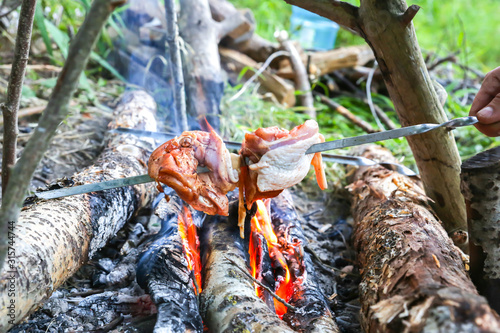 Man is frying chicken on the open fire. Grill in the forest. Tourist eating outdoors.