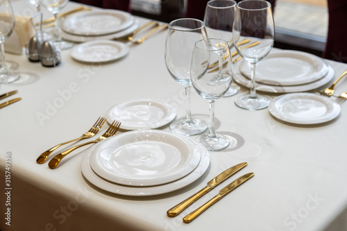 Chic and elegant, gold-plated cutlery and white plates, table setting with empty plates.