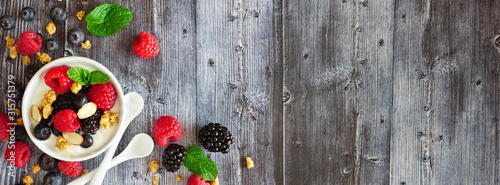 Healthy yogurt with fresh berries and granola. Banner with corner border against a rustic wood background. Copy space.