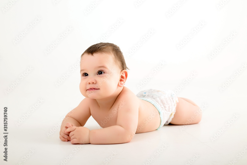 healthy baby brunette boy smiling and looking at the camera, baby in a diaper lying on a white background, space for text healthy baby brunette boy smiling and looking at the camera, baby in a diaper lying on a white background, space for text