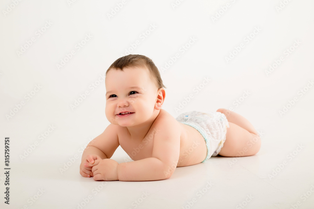 healthy baby brunette boy smiling and looking at the camera, baby in a diaper lying on a white background, space for text healthy baby brunette boy smiling and looking at the camera, baby in a diaper lying on a white background, space for text