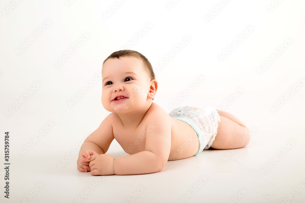 healthy baby brunette boy smiling and looking at the camera, baby in a diaper lying on a white background, space for text healthy baby brunette boy smiling and looking at the camera, baby in a diaper lying on a white background, space for text