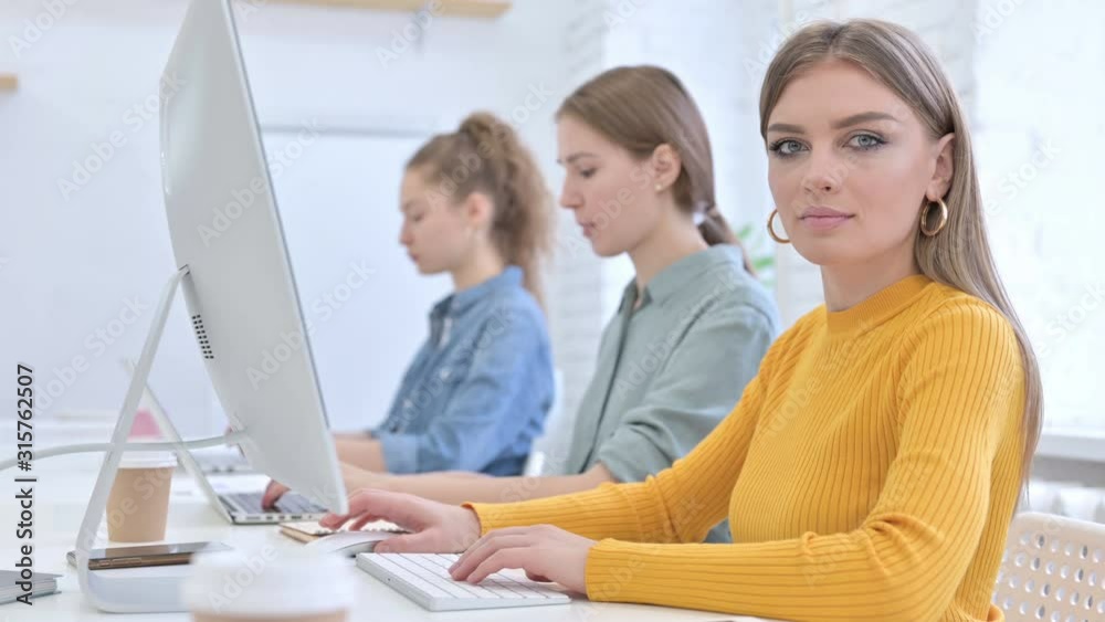 Young Female Designer working on Desktop and Looking at the Camera Young Female Designer working on Desktop and Looking at the Camera