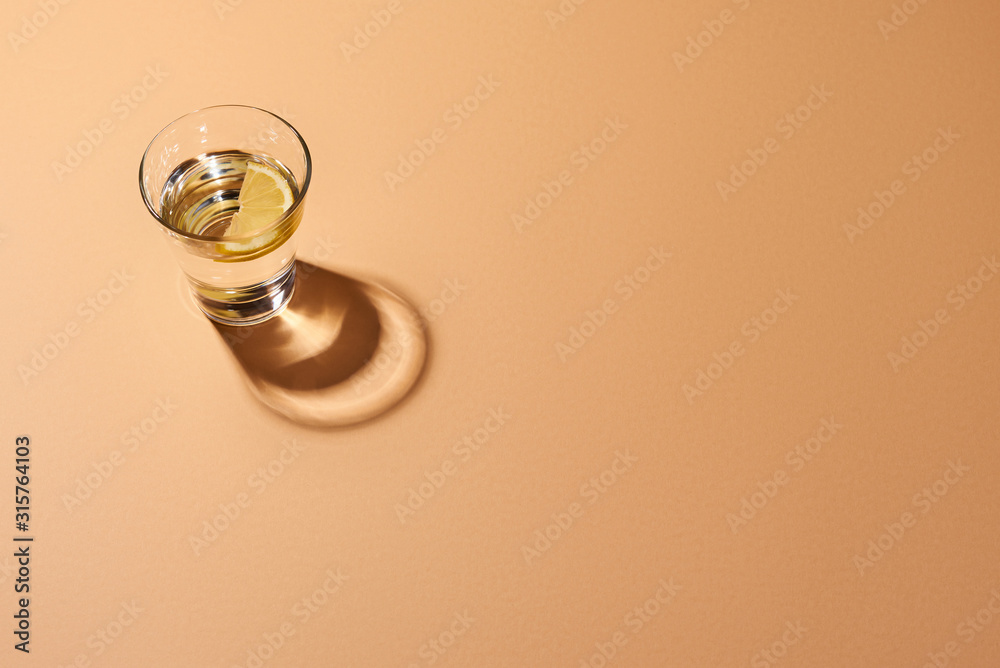 Glass of water with lemon on an orange surface. Top view.